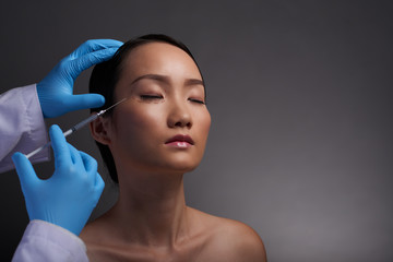 Chinese young woman having painful injections of hyaluronic acid