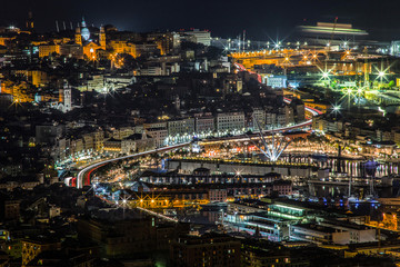 Traffic light trails in Genoa causeway, with skyline of the historic city center buildings and view of the port