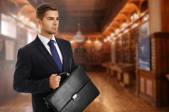 Businessman holding briefcase on blurred hall background. Law concept.