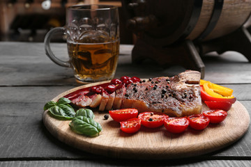 Grilled steak with tomatoes on cutting board and mug of beer, closeup