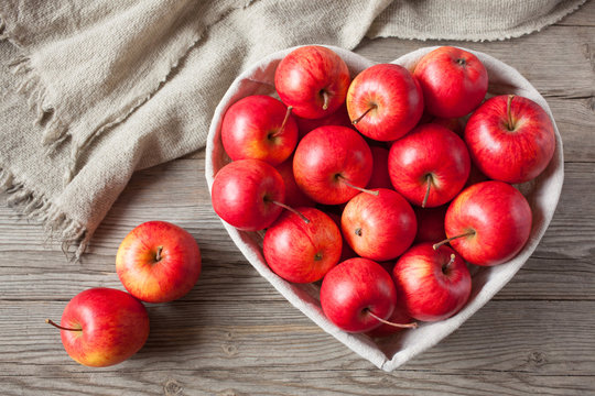 Red apples in the basket heart shape on wooden background