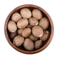 Nutmegs in a wooden bowl on white background. Myristica fragrans, also called pala, an edible brown and egg-shaped seed of a tree, culinary use as spice. Isolated macro photo close up from above.
