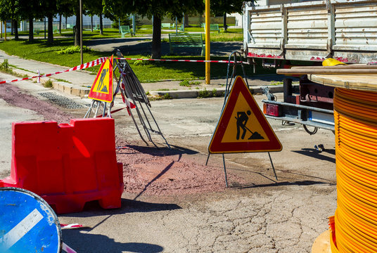 Warning signs for work in progress on road under construction. .fiber optic cables buried in a micro trench with concrete colored red by a worker