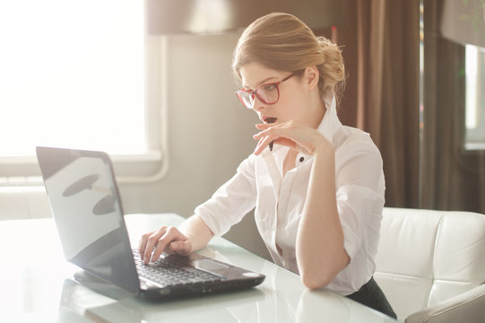 Portrait of a casual young businesswoman in blouse using laptop computer in office.