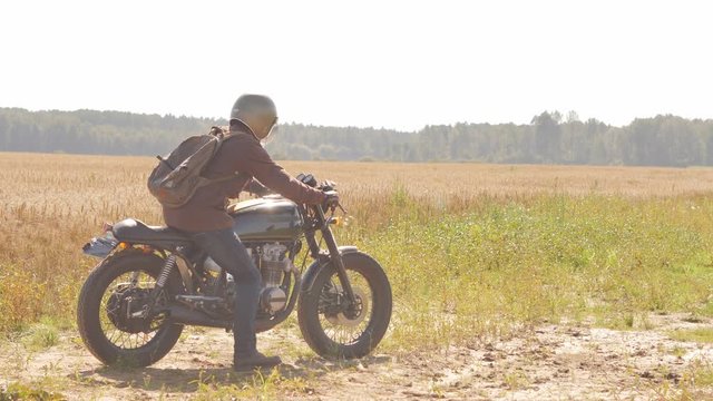 A man on the vintage custom cafe racer riding in a field.