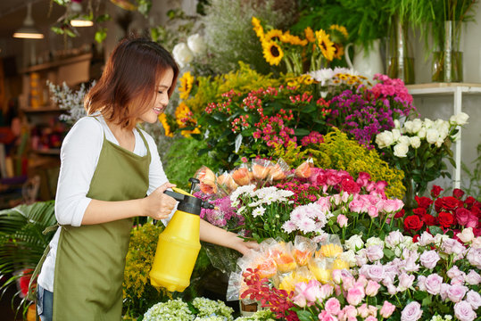 Vietnamese young flower shop owner spraying bouquets