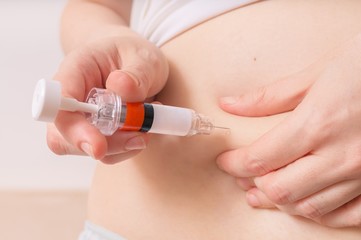 Diabetes and glycemia concept. Patient is injecting insulin injection to belly with syringe.