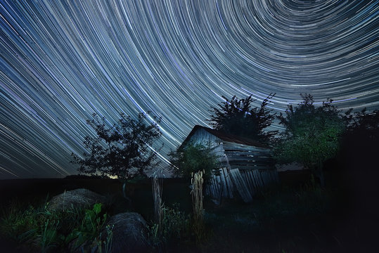 night photography sky star tracks on the background of an old wooden barn housing. Rural wilderness.
