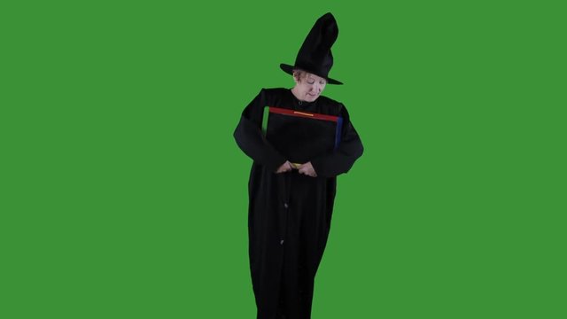 Woman dresses as witch for Halloween holding blank chalkboard sign against  freen background.