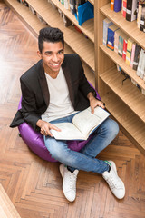 Top view of handsome man sitting on the floor near bookshelves and reading books in library.