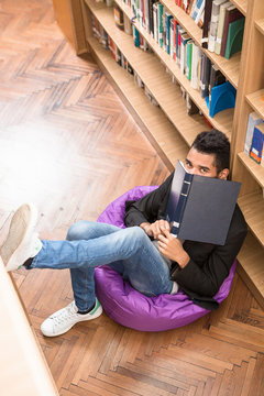 Top view of handsome man sitting on the floor near bookshelves and reading books in library.