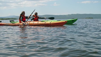 Tourist couple in orange safety vests rowing on clear lake on kayaks  - Powered by Adobe