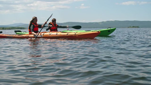 Tourist couple in orange safety vests rowing on clear lake on kayaks 