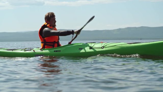 Man in life jacket rowing kayak on the lake with picturesque mountains in the background 