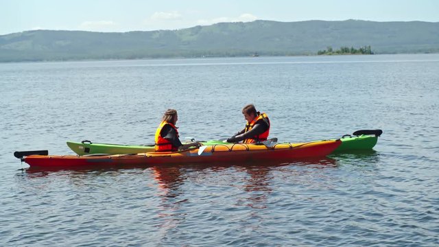 Woman posing with paddle in kayak while man photographing her with camera in the lake
