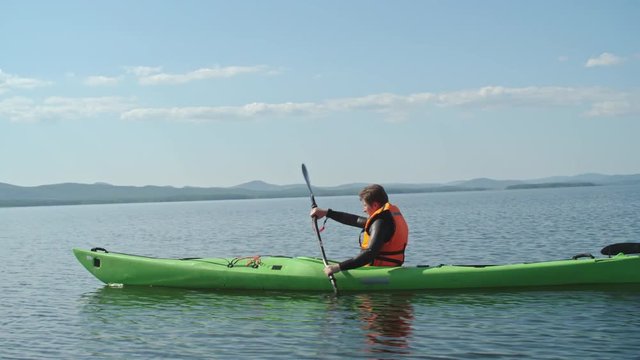 Side view of man in life jacket rowing a kayak on the lake in the summer