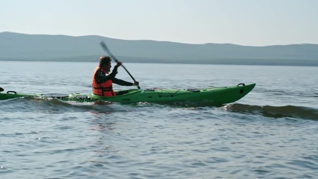 Sportsman in life jacket rowing a kayak on the lake with blue wavy water surface 