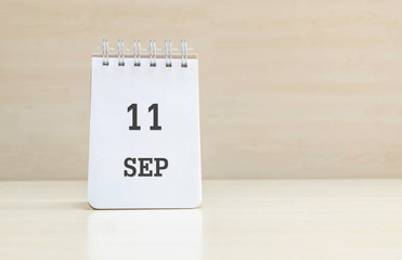 Closeup surface note book with black 11 sep word in page on blurred brown wood desk and wood wall textured background with copy space under window light