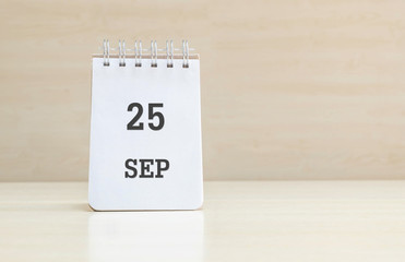 Closeup surface note book with black 25 sep word in page on blurred brown wood desk and wood wall textured background with copy space under window light