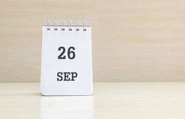 Closeup surface note book with black 26 sep word in page on blurred brown wood desk and wood wall textured background with copy space under window light