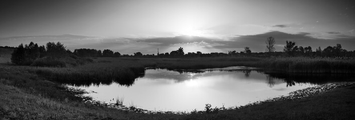  Village on banks of .river and beautiful rays of sun in sky. Panorama. Mirror reflection .in water. Black and white photo