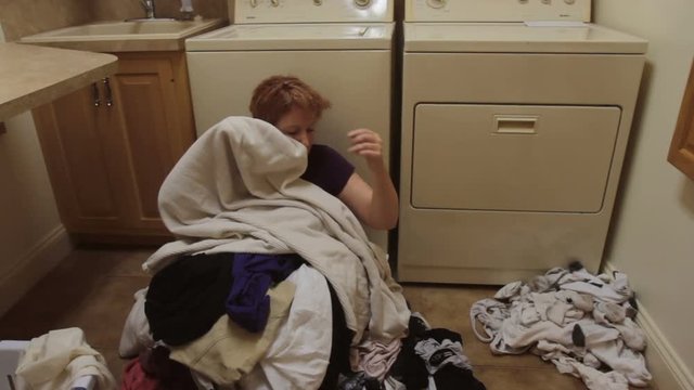 Woman buried under pile of dirty laundry in laundry room of home.
