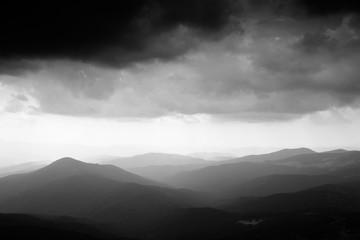 Mountain landscape. Mountain range in haze. Rays of light in lumen of mountains and clouds. Stormy weather. Panorama. Black and white photo