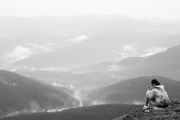 Girl with mobile phone on top of mountain. Mobile telephony, fast Internet in mountains. Chat on phone. Mountain landscape. Rain clouds, dramatic mood. Black and white photo