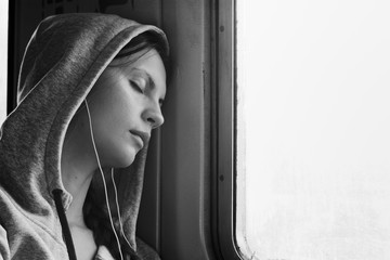 Sleeping girl in train. Portrait of beautiful brunette listens to music on trip. Journey by rail. Black and white photo