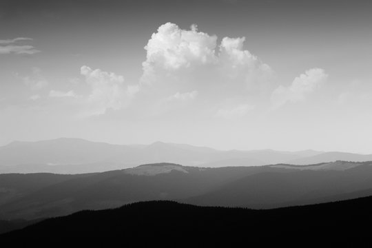 Mountain landscape in haze. Beautiful clouds in sky above mountain ridge. Stormy weather. Panorama. Black and white photo