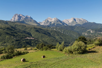 Fototapeta na wymiar Haystacks lying in green fields with the Apennines ridge in the background, Abruzzo, central Italy
