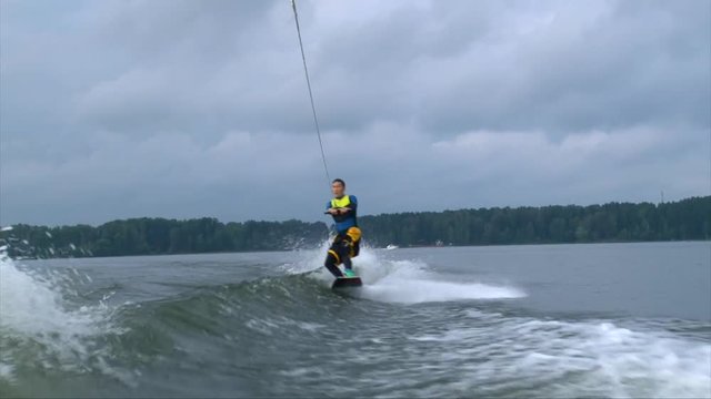 A young asian man jumps the wake behind a boat, wakeboarding in cold water