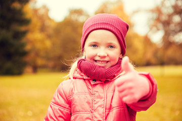 happy little girl showing thumbs up in autumn park