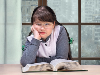 Girl with the book is sad. Outside the window, snow, winter. The concept of sadness, loneliness,...
