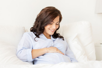 Naklejka premium happy pregnant woman lying on bed at home