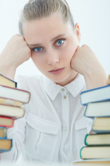 Tired female student at workplace taking nap on pile of books.