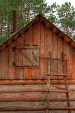 Ladder and a near the wall of a wooden hut with a loft on a background of the forest.