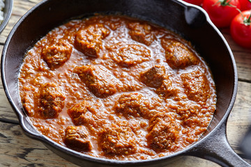 Madras butter beef curry slow cook Indian spicy lamb food in cast iron pan on vintage wooden table background. Traditional India culture restaurant dish.