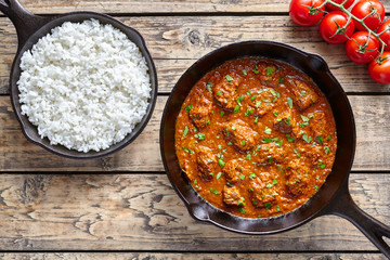 Beef Madras traditional slow cook Indian spicy chili lamb meat food with rice and tomatoes in cast iron pan on vintage wooden table background. India culture restaurant dish.