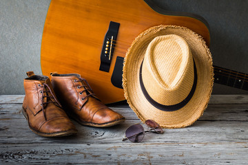 Boots with brown hat, sunglasses and guitar on wooden table over grunge background