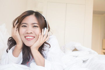 Asian woman listening to music on headphones on bed at room