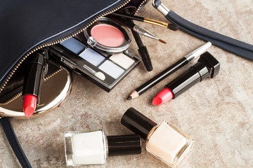 Maquillaje junto a un bolso de mujer sobre un fondo gri. Vista superior y de cerca