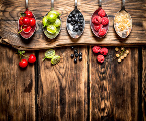 Different berries spoons. On wooden background.