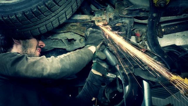 Bright sparks coming from grinder tool cutting rusty worn car part.