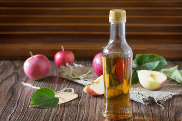 Apple cider vinegar in a glass bottle with fresh apples on a tab