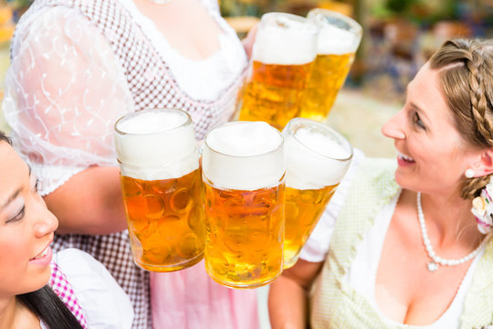 Kellnerin im Dirndl serviert Bier in fünf Maßkrügen an zwei Frauen
