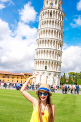Young female traveler having fun in front of the famous leaning tower in Pisa old town in Italy....