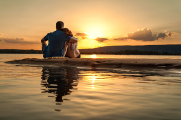 Beautiful couple is sitting on the beach and looking at the suns