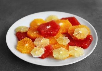 Plate with different citrus slices on grey background