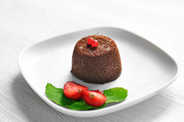 Tasty chocolate fondant with red currant and strawberry on white plate, closeup